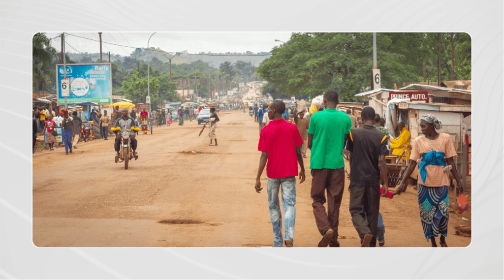 City street in Bangui, Central African Republic, filled with people walking and vehicles traveling down the road.