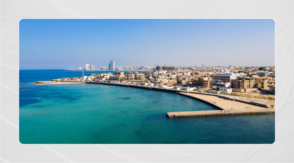 Photo of coastal shore in Benghazi, Libya featuring clear blue water and a surrounding city.